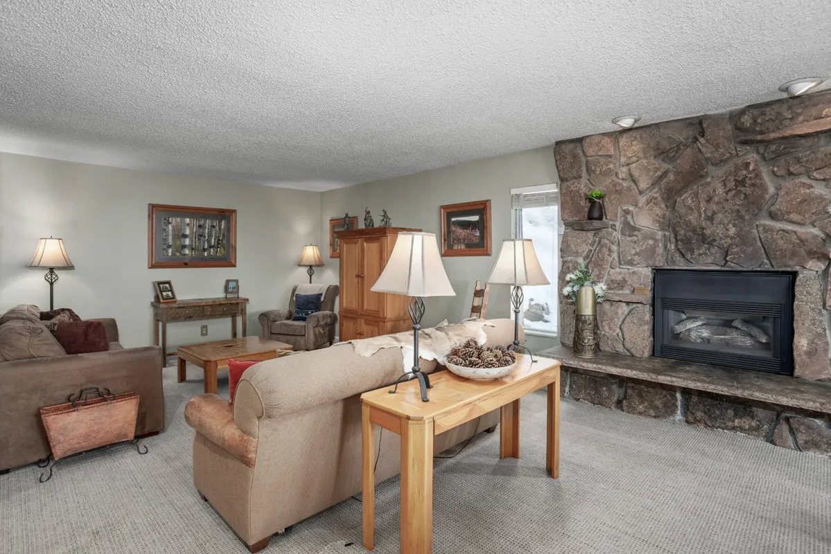 A cozy living area featuring a stone fireplace, comfortable sofa seating, and warm lighting from lamps. The stone fireplace creates a snug ambiance, ideal for relaxing after a day outdoors, especially in winter.