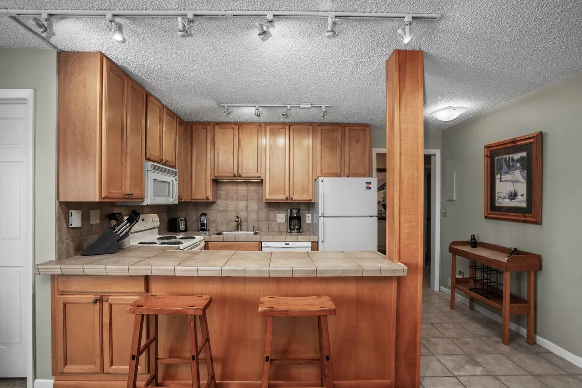 A modern, well-equipped kitchen featuring a central island with wooden bar stools, ample cabinetry, and high-quality appliances. The open layout encourages socializing and group cooking, with plenty of space for guests to gather and participate.