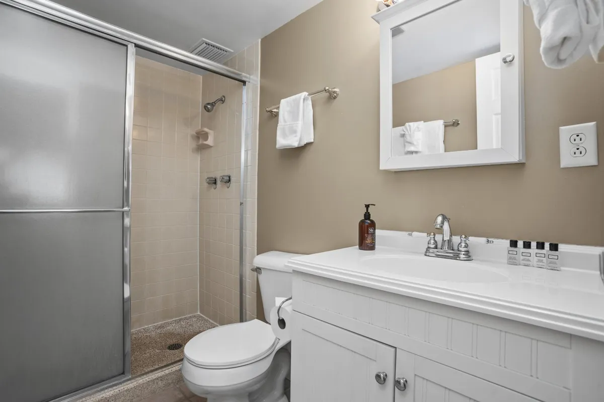 A modern bathroom showcasing a sleek vanity with sink, large mirror, and a walk-in shower area. The design is fresh and inviting, reflecting ample space for personal comfort and grooming.