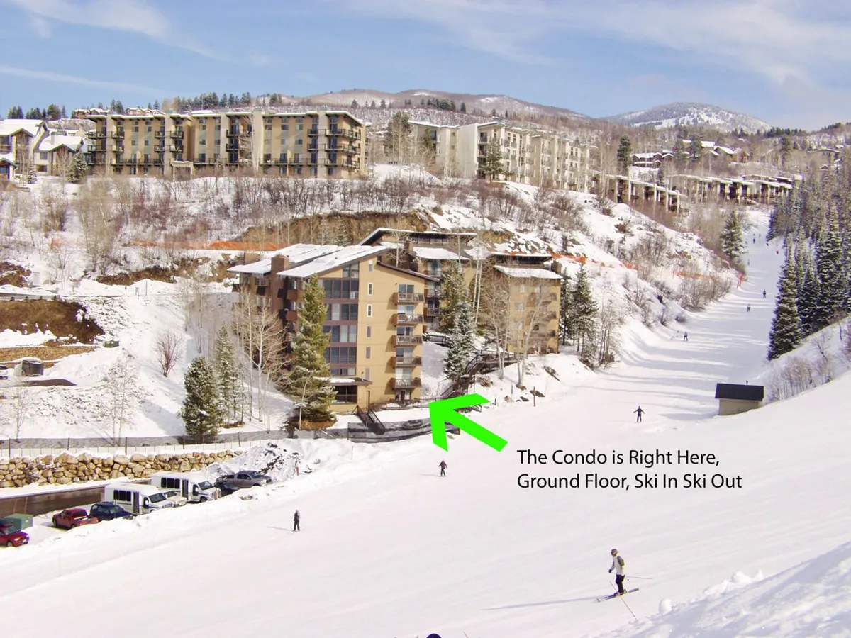 The exterior of the condo building highlighted against a snowy backdrop, with skiers on the slope right outside. The scenic mountain view, ski slope, and building proximity reinforce the property's direct ski-in/ski-out access and its unique location at the base of the mountain.